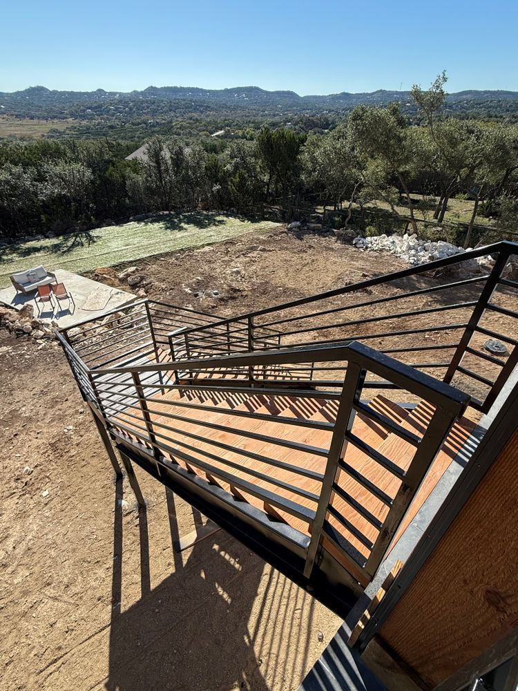 Staircase with black railings overlooking a dry hillside and distant mountains under clear sky