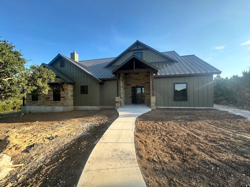 Modern single-story house with a metal roof, stone accents, and a concrete walkway in a dry yard.