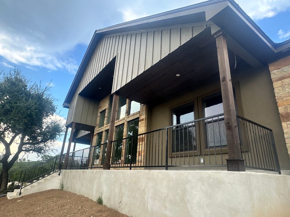 Modern house exterior with a covered porch, wooden columns, and black railing on a sloped foundation