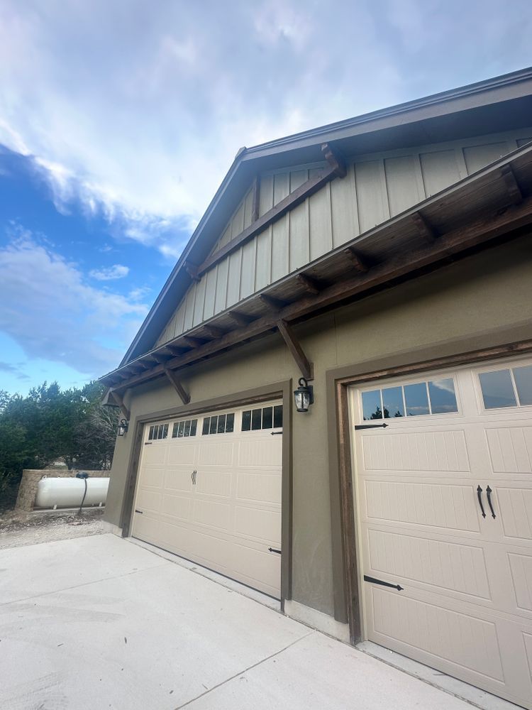 Two beige garage doors on a house exterior under a blue sky