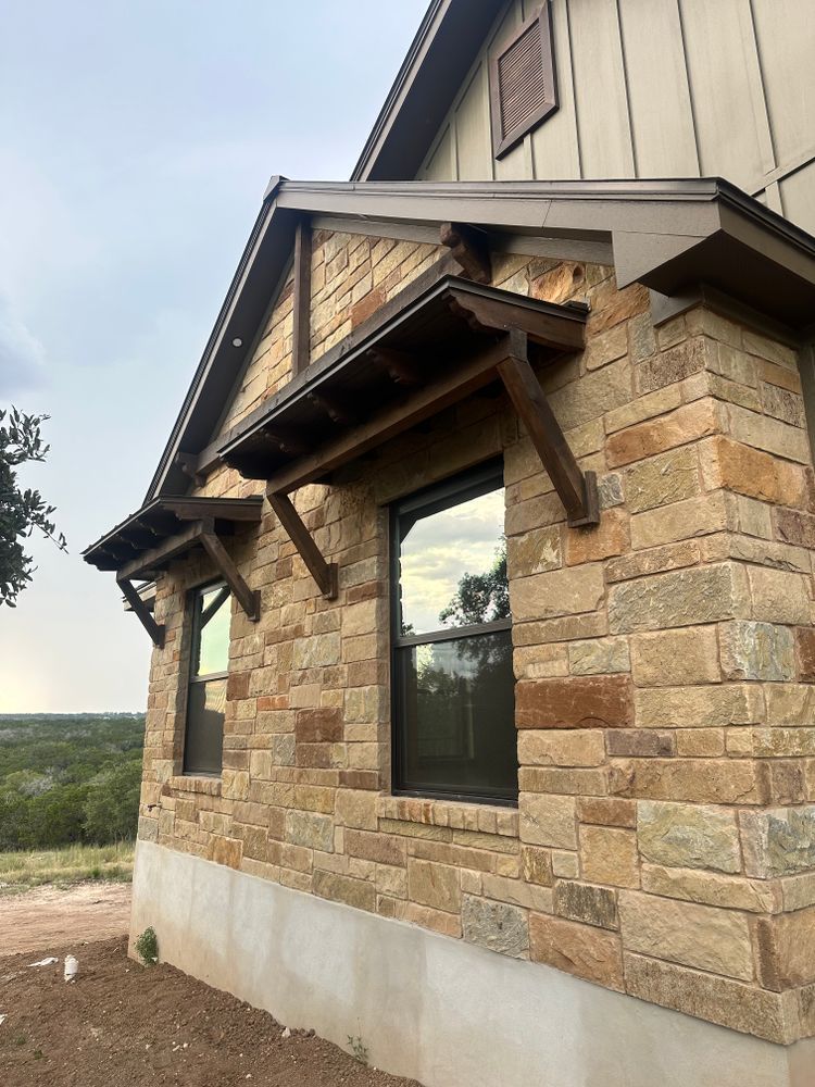 Stone house exterior with a gabled roof, wooden awning, and dark-framed window