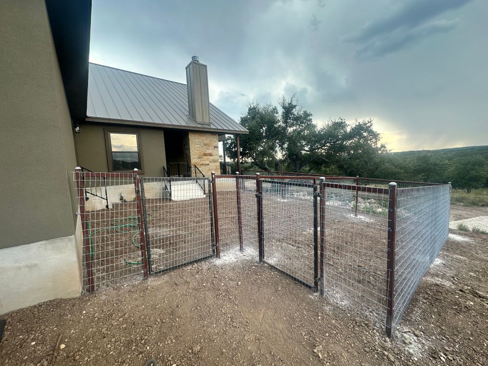 Wire mesh fenced enclosure beside a house, with a gravel ground and cloudy sky.