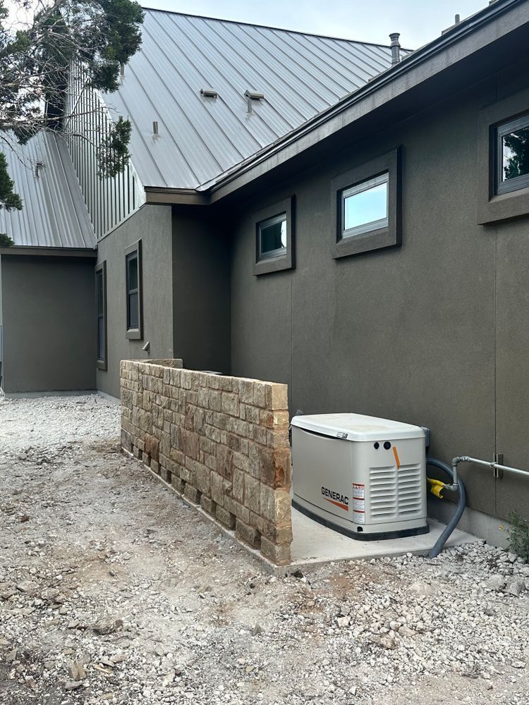 Outdoor HVAC unit beside a gray building and stone privacy wall on a gravel path.