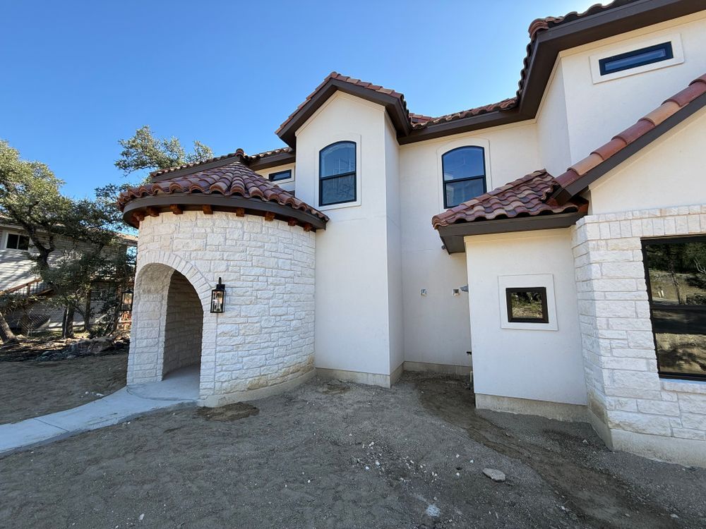 White stucco house with red-tiled roofs, arched entry, and blue sky in the background