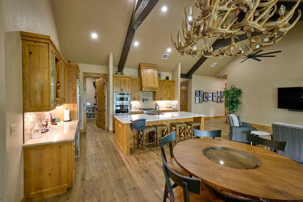 Warm wood kitchen and dining area with island, pendant lights, and round table under a chandelier.