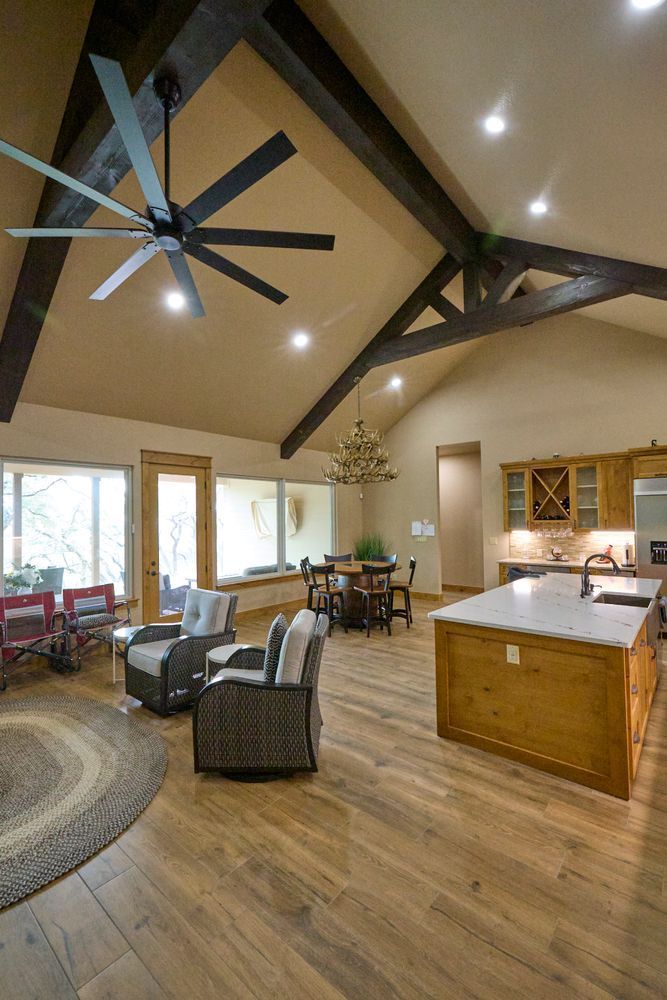 Spacious open-plan living room with vaulted wood ceiling, ceiling fan, fireplace, and kitchen island