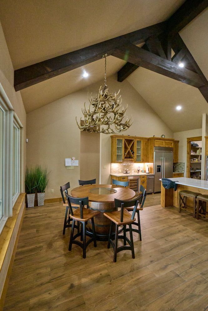 Rustic dining room with wooden beams, round table, chairs, chandelier, and open kitchen counter