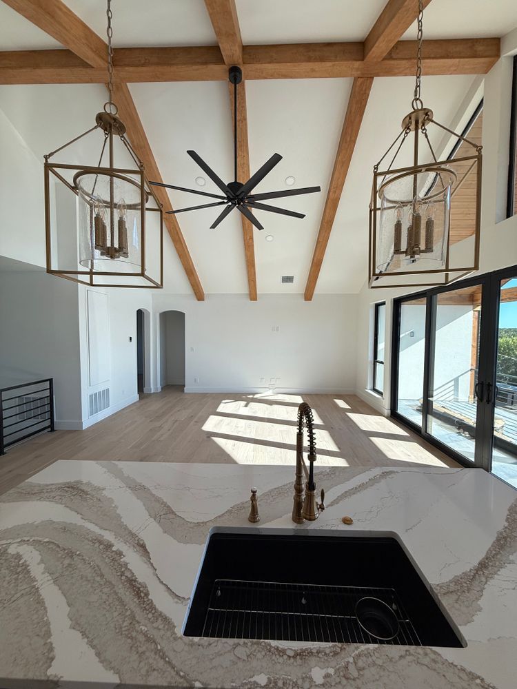 Bright living room with exposed wood beams, large windows, ceiling fan, and kitchen island sink.