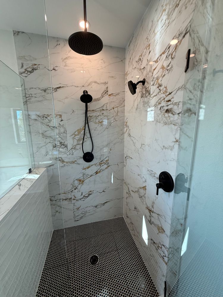 Modern bathroom shower with white marble tile, black fixtures, and patterned floor.