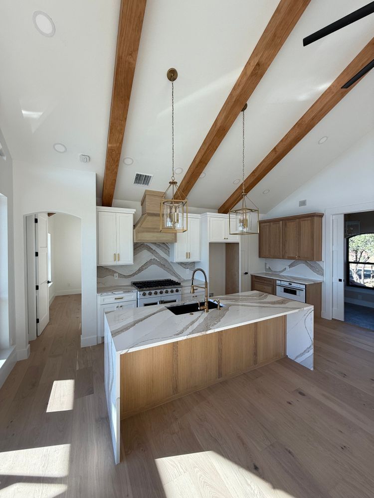 Bright modern kitchen with white cabinets, wood beams, island sink, and hardwood floors