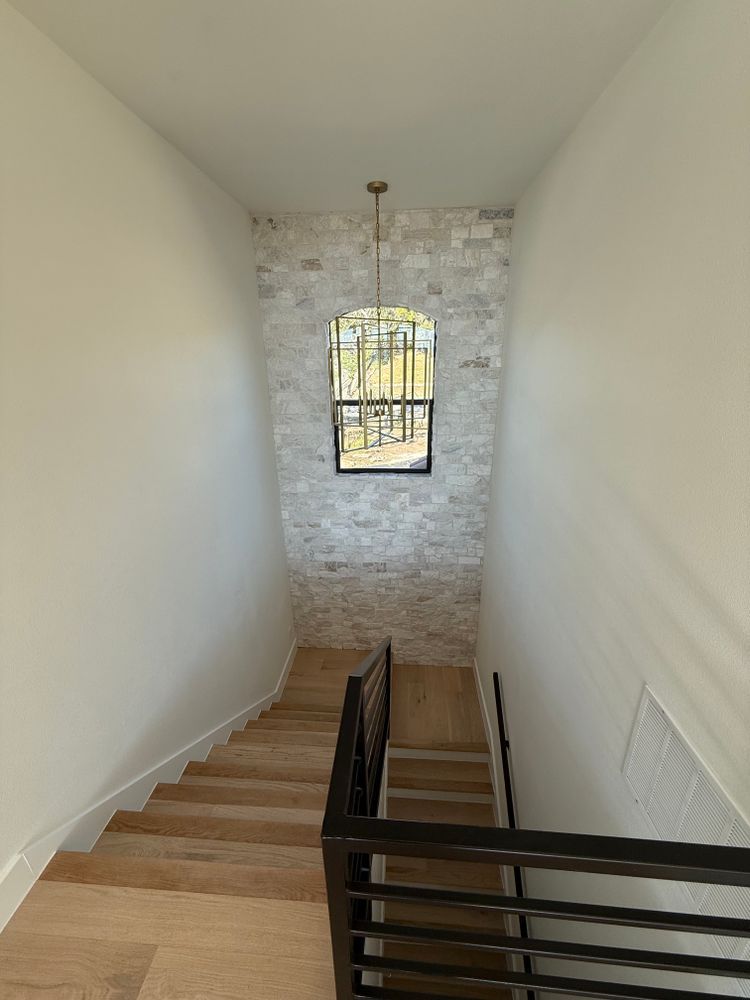 Narrow staircase with wooden steps, white walls, and a small window at the bottom.