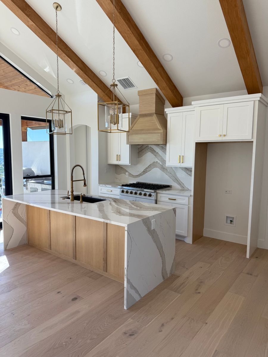 Modern kitchen with wood beams, white cabinetry, marble island, and stainless steel appliances