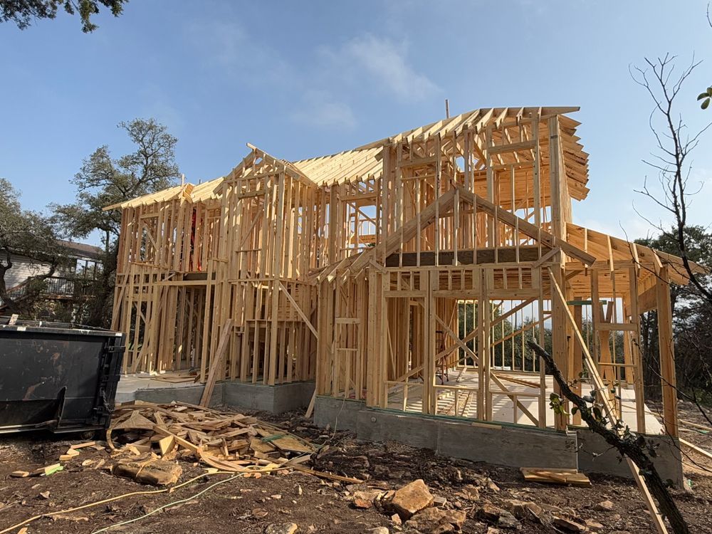 Wood-framed house under construction with exposed lumber and roof trusses on a cleared lot