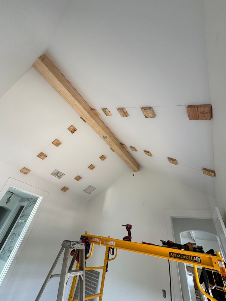 Renovation work in a white room with exposed ceiling beams, ladder, and yellow lifting equipment