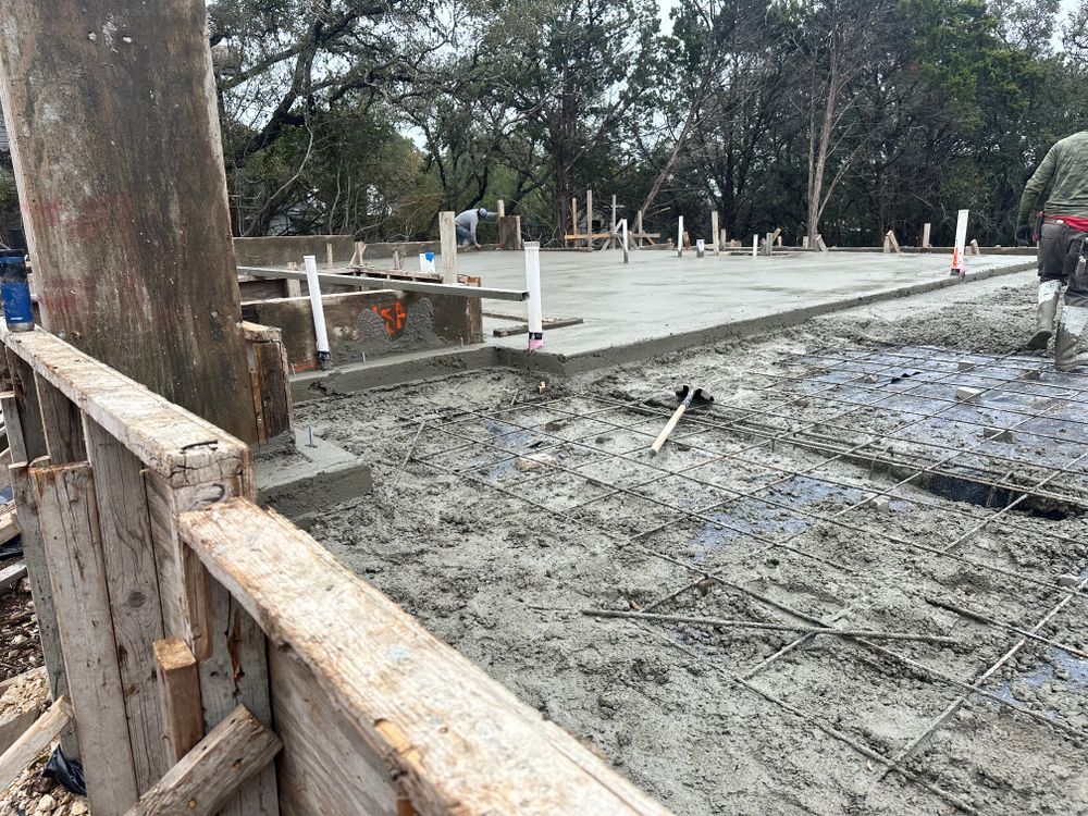 Concrete being poured and smoothed at an outdoor construction site with wooden forms and trees nearby