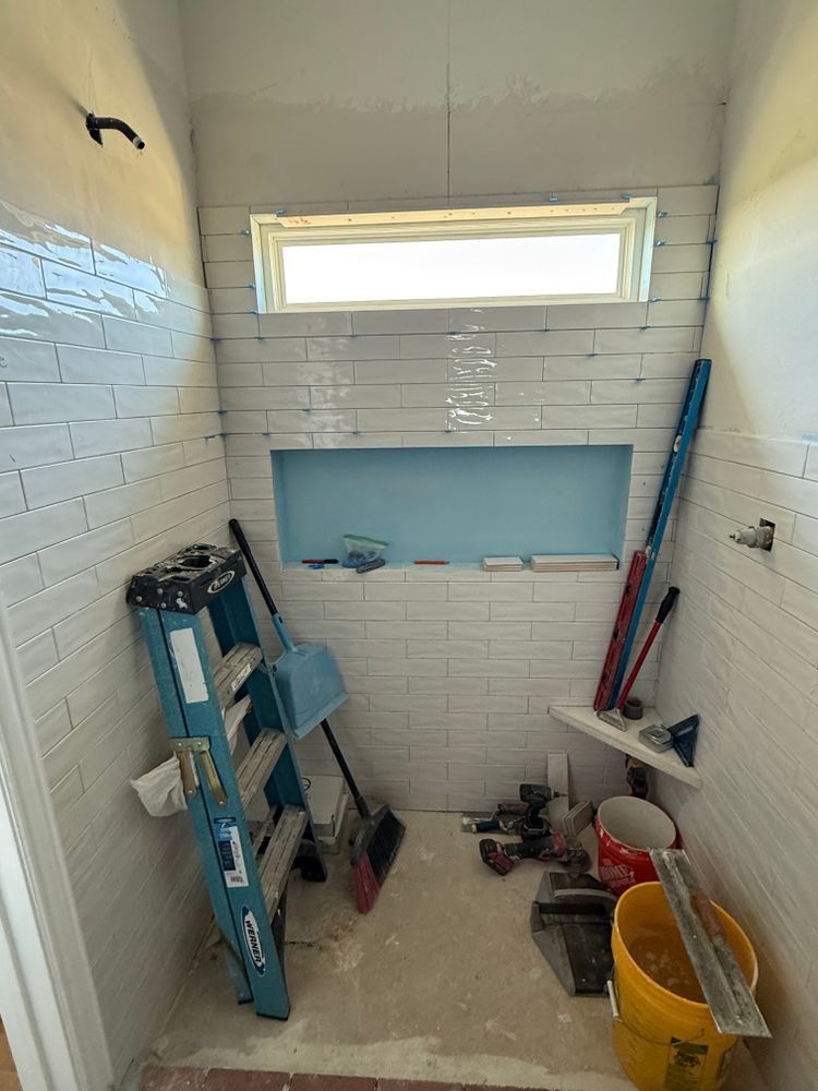 Small white-tiled shower stall with ladder, bucket, tools, and cleaning supplies on the floor.