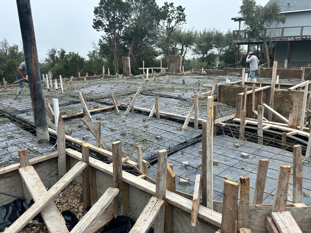 Construction site with concrete foundation forms, wooden supports, and workers on a muddy, overcast day