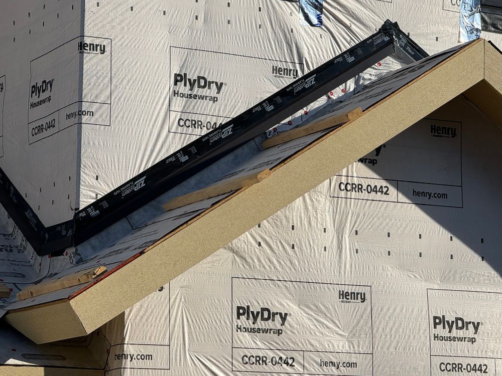Partially installed roof vent flashing on house sheathing, with black and tan trim pieces.