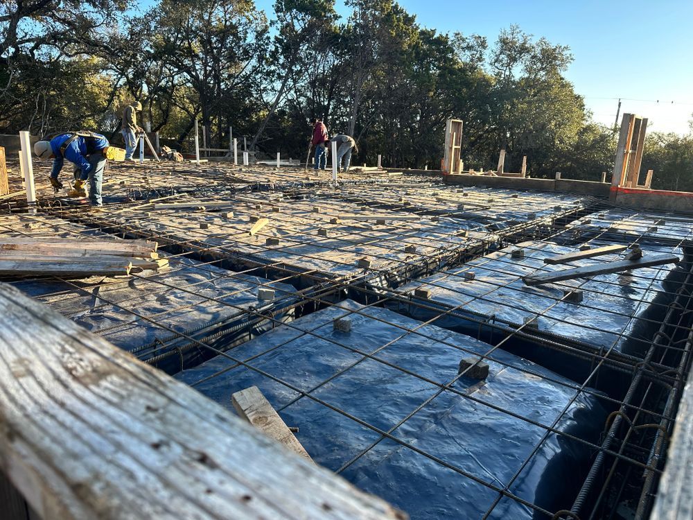 Construction site with workers pouring concrete over rebar and wooden forms outdoors