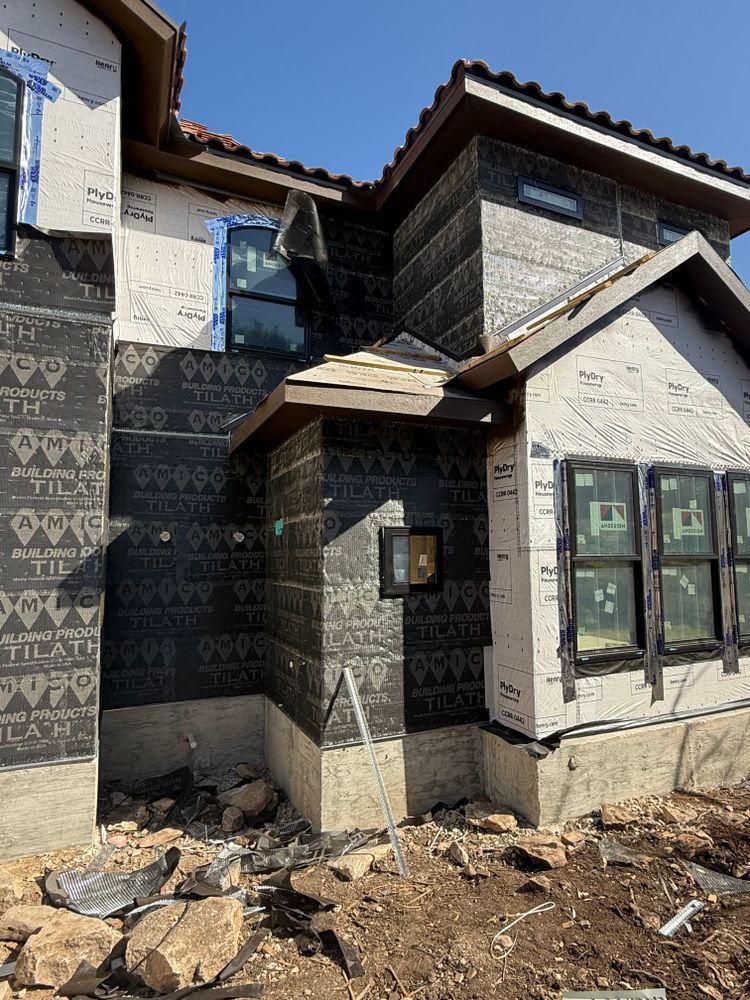 Partially finished house exterior with stucco walls, dark trim, and exposed dirt in front