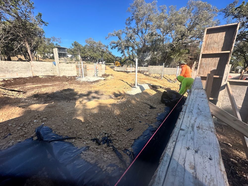 Construction site with dirt lot, concrete walls, and a worker in an orange shirt along a long wooden form.