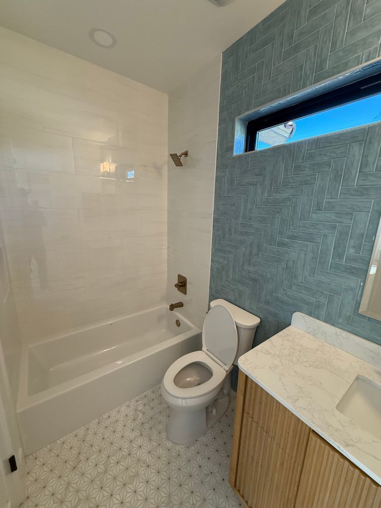 Modern bathroom with white tub, toilet, and blue accent wall beside a vanity.
