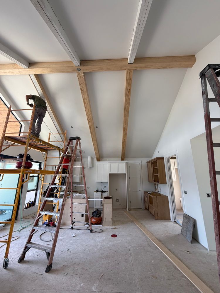 Renovation in progress in a room with ladders, exposed ceiling beams, tools, and construction materials.