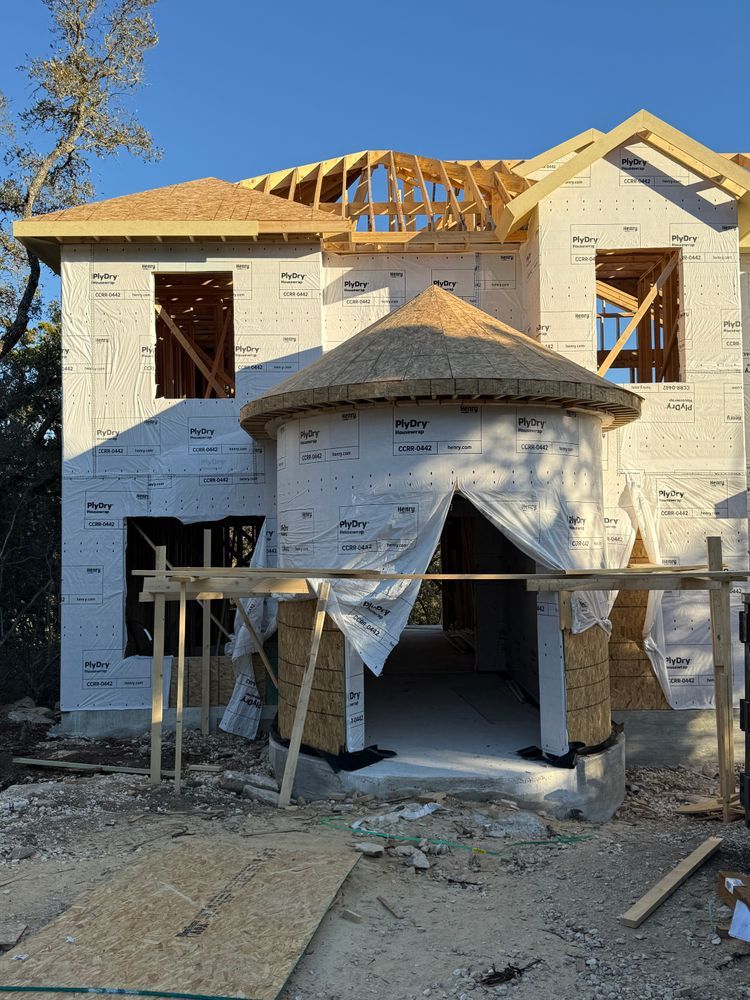 Partially built two-story house with white wrap, exposed framing, and stone entry porch under construction