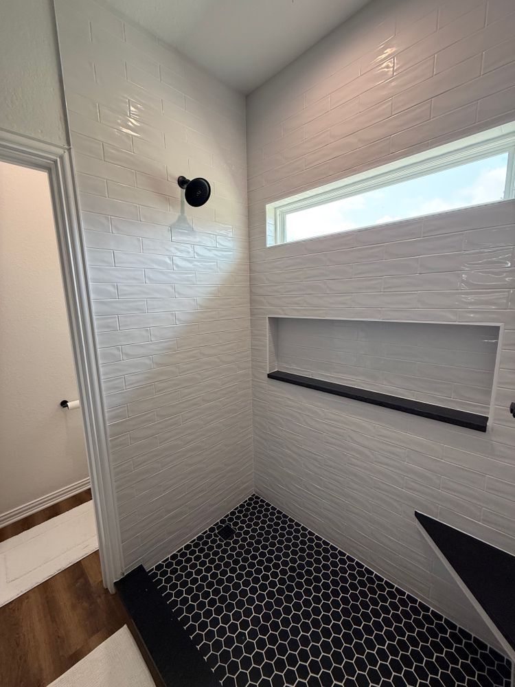 Modern bathroom shower with white textured walls, black hex tile floor, and a narrow horizontal window.