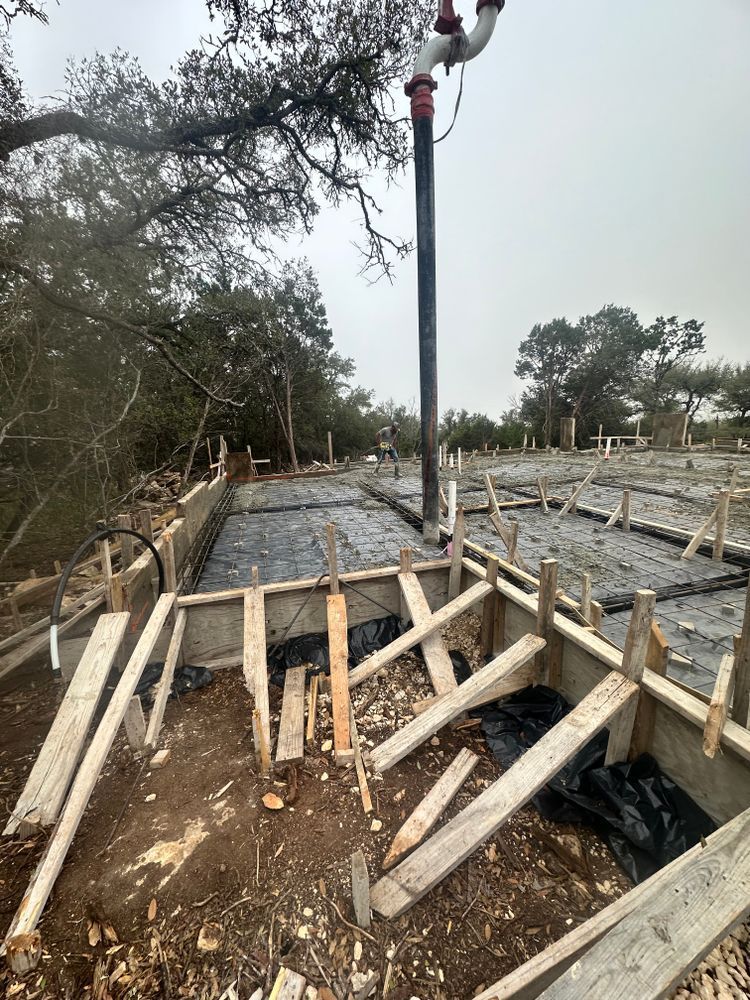 Construction site with rebar and concrete forms for a foundation, surrounded by debris and trees