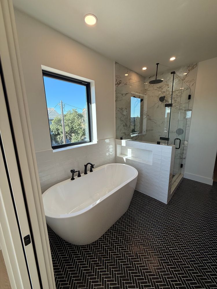 Modern bathroom with freestanding tub, walk-in glass shower, and black patterned tile floor.