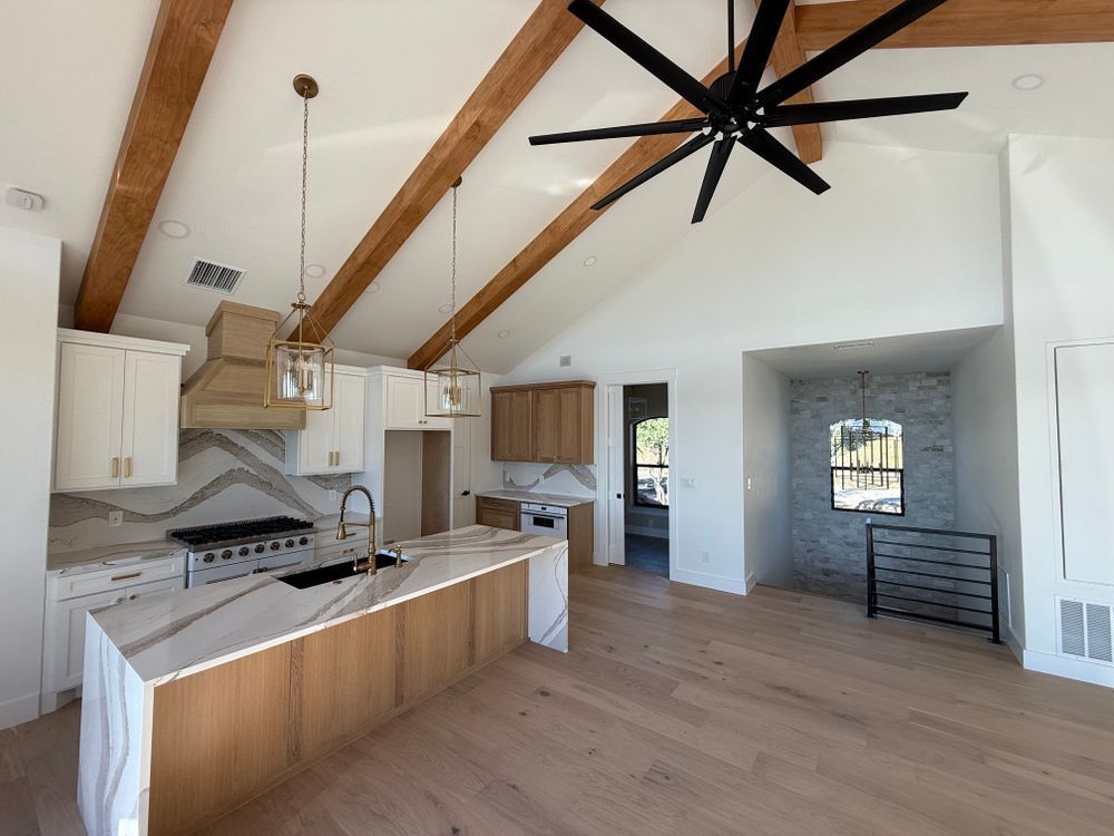 Bright open kitchen and living area with wood beams, white cabinets, island, and large ceiling fan