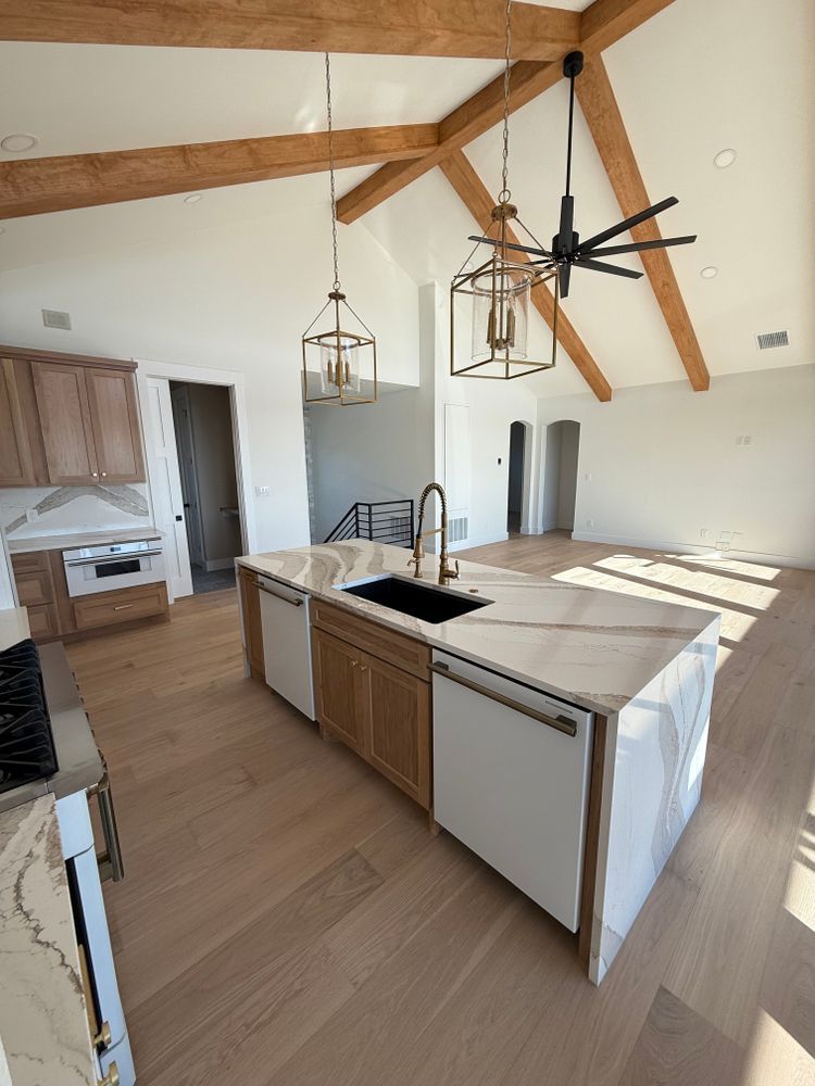Modern kitchen with wood beams, white island, pendant lights, and large windows overlooking a bright room
