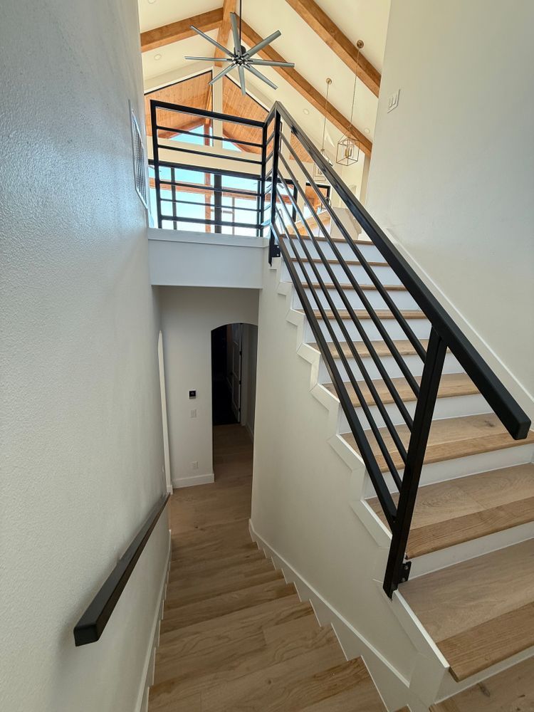 Staircase with white walls, wood steps, black railing, and vaulted ceiling with exposed beams