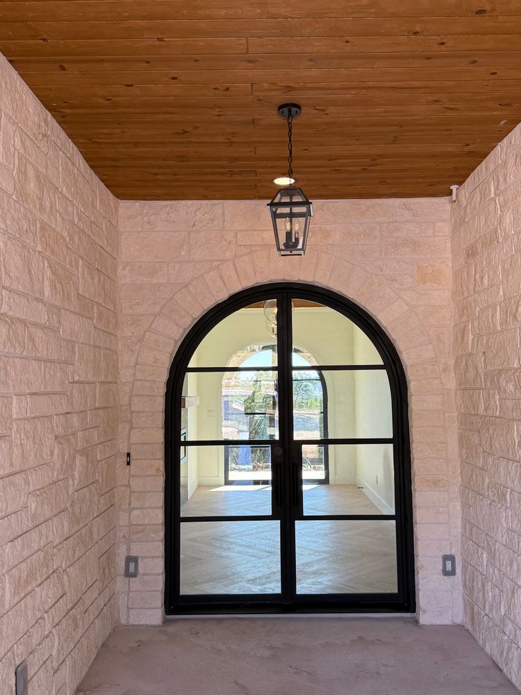 Arched doorway leading to a bright courtyard, with stone walls, wood ceiling, and hanging lantern.