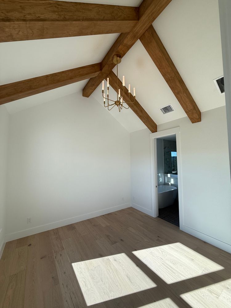 Empty white room with exposed wooden beams, hanging light fixture, and sunlight on the floor