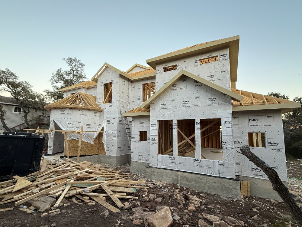 Partially built house wrapped in white housewrap, with piles of lumber and debris in front