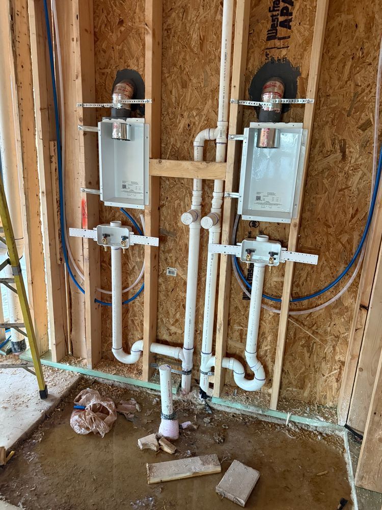 Two wall-mounted utility boxes and white pipes in an unfinished room with exposed studs and OSB walls