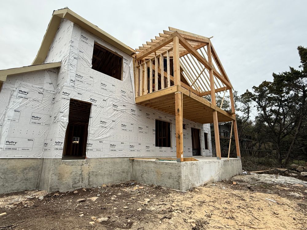 Partially built white house with exposed wooden frame on a dirt lot under cloudy skies
