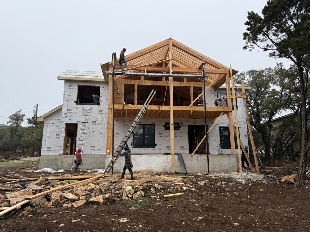 House under construction with workers on the roof and ladders against the frame