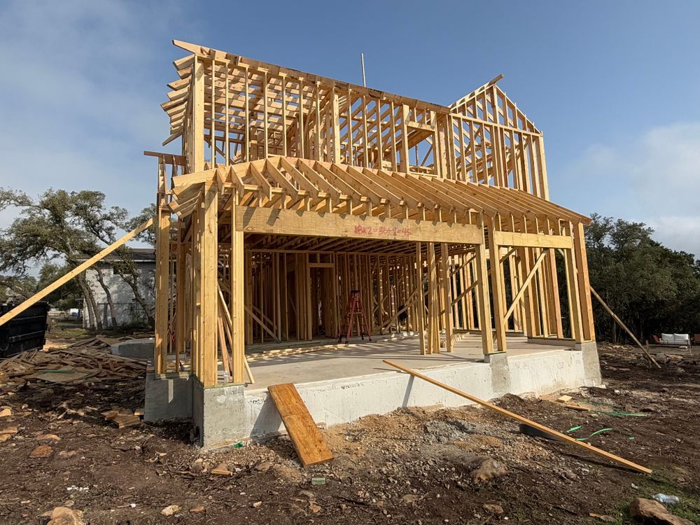 Framed house under construction with exposed wooden beams and a concrete foundation