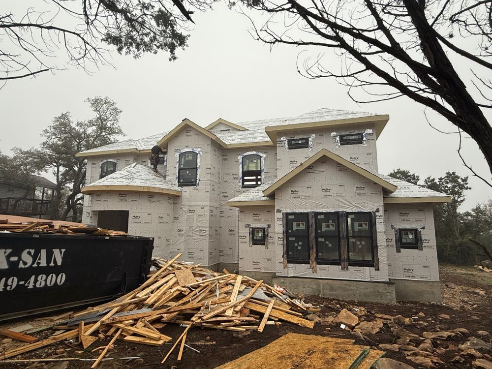 Partially built white two-story house with construction debris and a dumpster in front