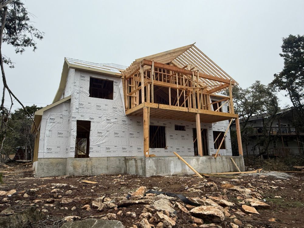 Partially constructed house with white sheathing and exposed wooden framing on a rocky lot