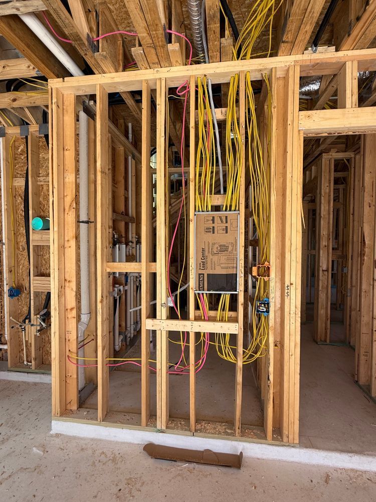 Unfinished house wall framing with electrical wiring and breaker panel installed.