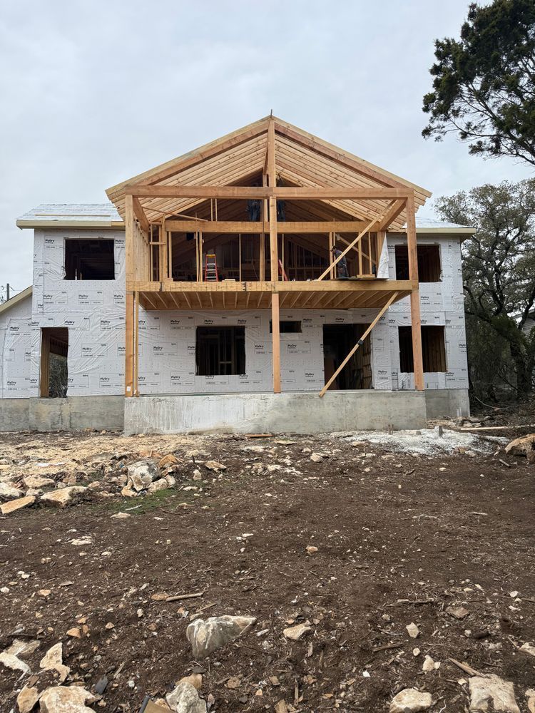 Partially built two-story house with exposed wooden framing and unfinished brick walls on a dirt lot