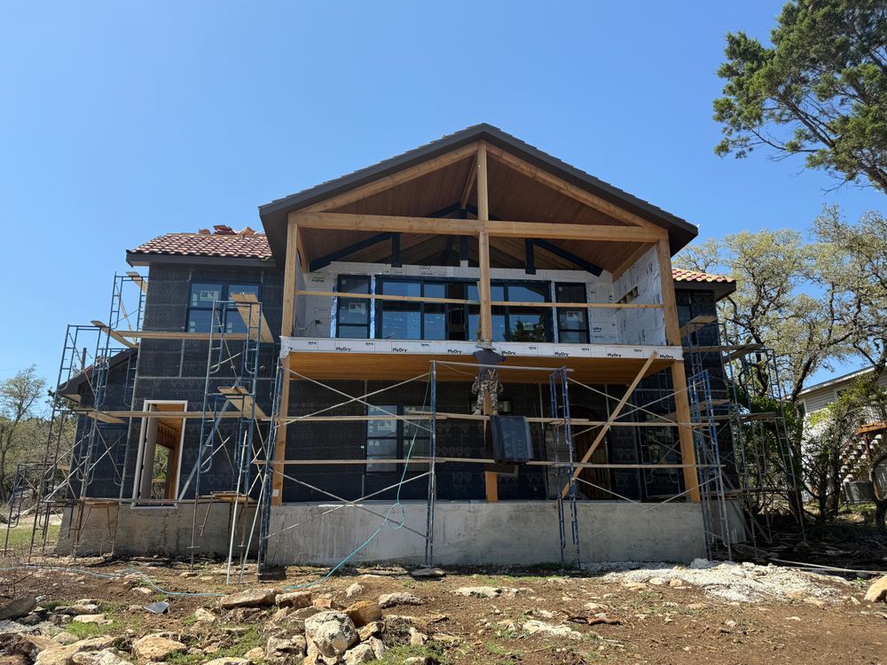 House under construction with scaffolding and exposed wooden roof framing under a clear blue sky