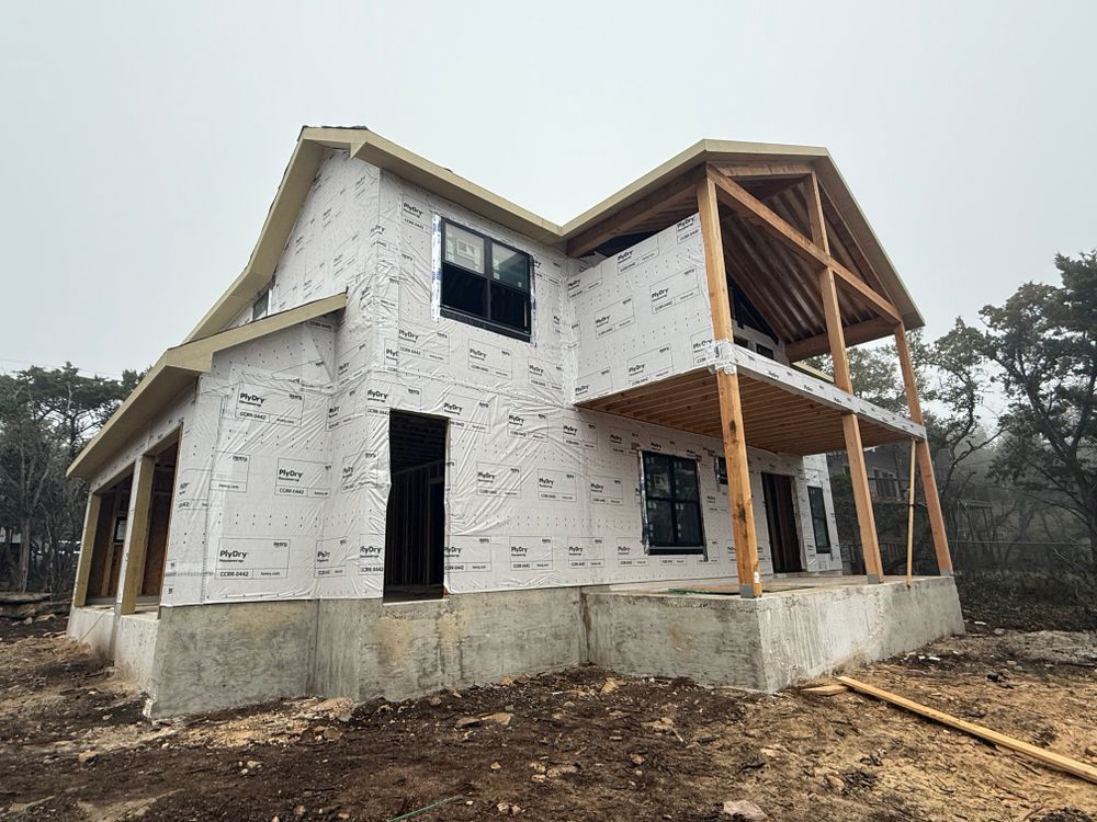 Partially built house wrapped in white sheathing with exposed wooden porch and concrete foundation