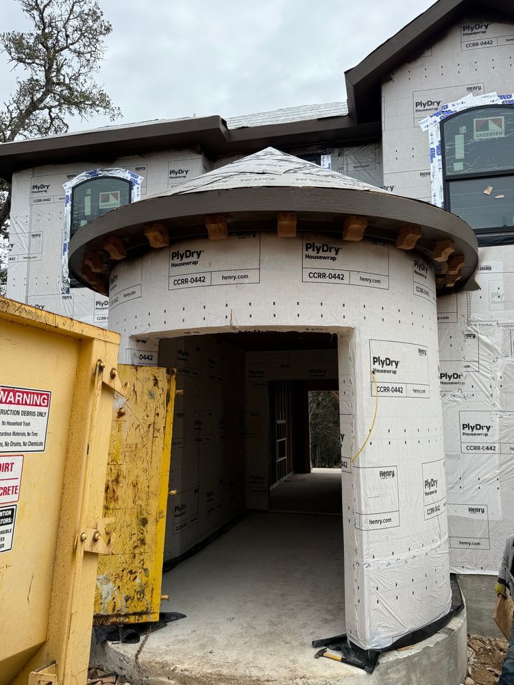 Front entrance of a house under construction, with white sheathing and a curved wood-framed overhang.