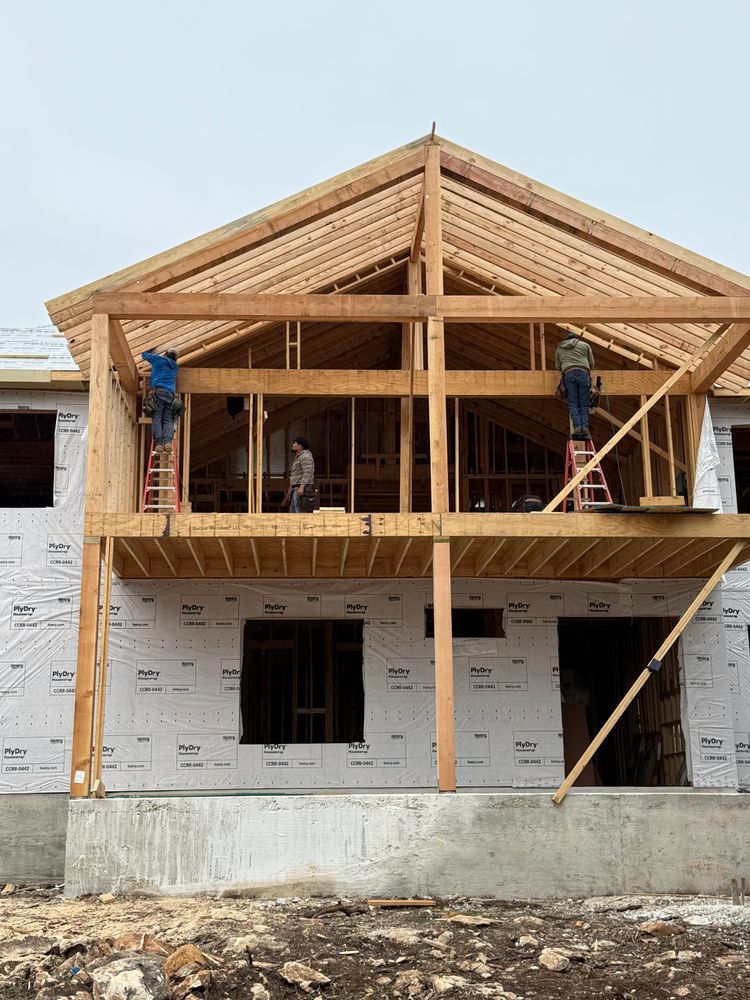 Wooden house frame under construction with two workers on the upper level and white wrap on the lower exterior
