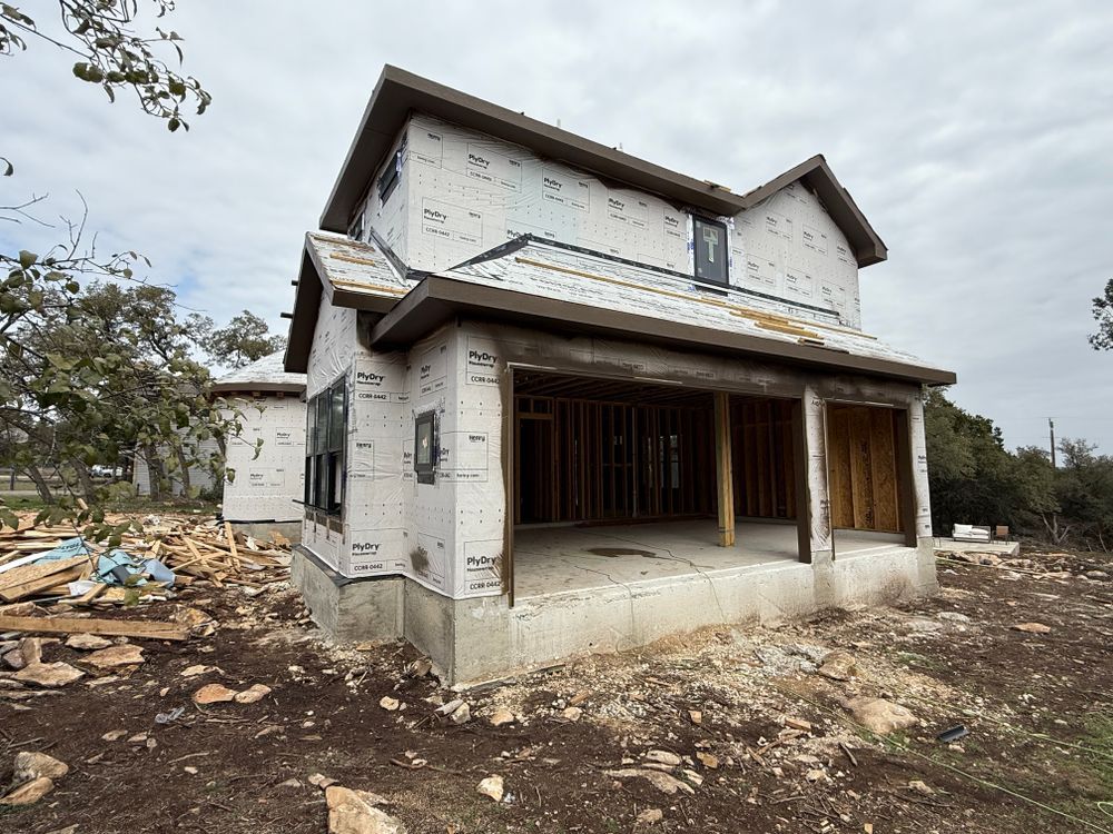 Unfinished two-story house with white exterior and covered porch on a bare, debris-strewn lot.